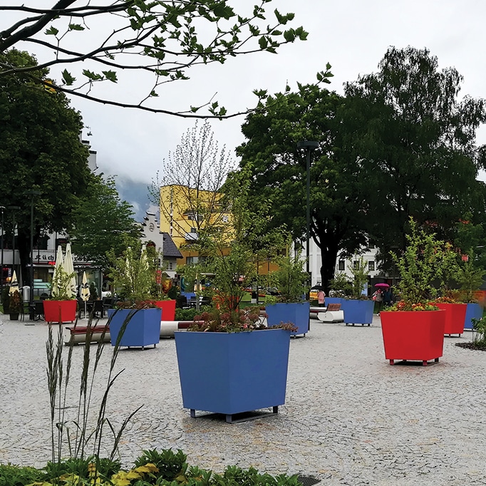 Jardinera urbana tipo palmera con revestimiento en polvo azul y rojo producida por CYRIA para el reverdecimiento de plazas públicas.